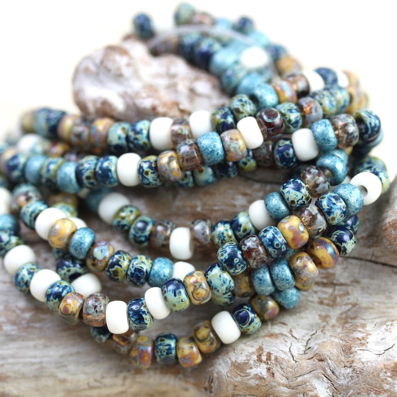May include: A close-up of a strand of blue, white, and brown seed beads. The beads are arranged in a random pattern and are strung on a clear thread.