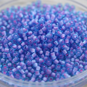 May include: A close-up of a bowl filled with small, round, blue and purple glass beads. The beads have a translucent finish and a slight iridescent shimmer.