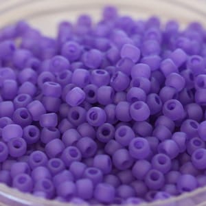 Könnte beinhalten: Nahaufnahme eines Haufens kleiner, matter, lila Perlen. Die Perlen sind zylindrisch mit einem Loch in der Mitte. Die Perlen sind verstreut, füllen den Rahmen aus und scheinen aus Glas oder einem ähnlichen Material zu bestehen.