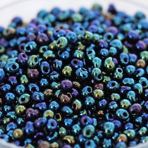 May include: A close-up of a pile of iridescent blue seed beads. The beads have a metallic sheen and are perfect for jewelry making.