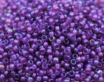 May include: A close-up image of a large quantity of small, round, iridescent purple beads. The beads have a metallic sheen and are perfect for jewelry making.