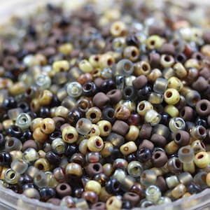 May include: A close-up of a variety of small glass beads in shades of brown, beige, and gray. The beads are arranged in a random pattern and are perfect for jewelry making or other craft projects.