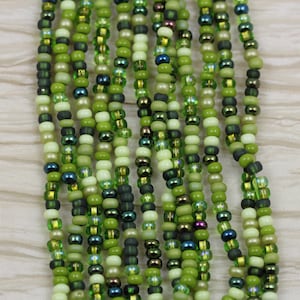 May include: A strand of green, cream, and dark green seed beads. The beads are arranged in a repeating pattern.