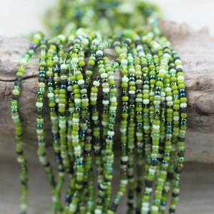 May include: A strand of green, white and black seed beads. The beads are small and round, and they are strung together in a random pattern.