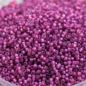 Può includere: Una vista ravvicinata di una grande quantità di piccole perline rotonde di colore rosa. Le perline hanno un riflesso metallico e sono sparse in un mucchio.