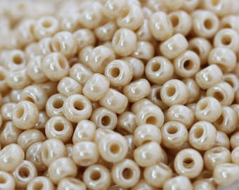 May include: A close-up shot of a pile of small, off-white, round beads. Each bead has a hole running through the center. The beads have a pearlescent sheen, reflecting light. These beads are suitable for jewelry making and crafts.