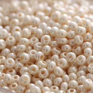 May include: A close-up of a large quantity of small, round, off-white beads. The beads have a smooth, glossy finish.