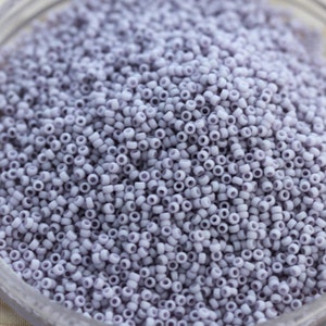 May include: A close-up view of a large quantity of small, round, light purple beads. The beads are arranged in a random pattern and fill the entire frame.