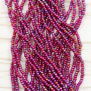 Puede incluir: Primer plano de una hebra de pequeñas cuentas de semillas de color rosa iridiscente. Las cuentas están dispuestas en una pila suelta, mostrando su superficie reflectante.