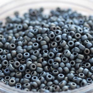Może przedstawiać: Zbliżenie na stos małych, okrągłych, ciemnoszarych koralików. Korale mają matowe wykończenie i są idealne do tworzenia biżuterii.