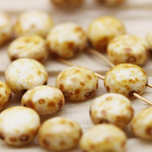 May include: A close-up of a collection of white and brown speckled beads. The beads are round and have a smooth, polished finish.