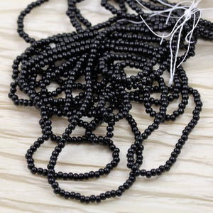 Puede incluir: Primer plano de un montón de cuentas de semillas negras. Las cuentas son pequeñas y redondas, y están dispuestas en un patrón aleatorio.