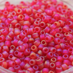 Könnte beinhalten: Nahaufnahme eines Haufens kleiner, runder, rosa und goldfarbener, irisierender Glasperlen. Die Perlen sind undurchsichtig und haben eine leicht matte Oberfläche.