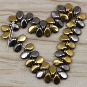 May include: A strand of teardrop-shaped beads in gold and silver tones. The beads are arranged in a pattern of alternating colors.