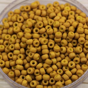 May include: A close-up image of a bowl filled with small, round, yellow beads. The beads are opaque and have a slightly matte finish.