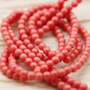 May include: A strand of coral-colored beads, made of a smooth, matte material. The beads are round and uniform in size, creating a consistent look.