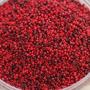 May include: A close-up image of a large quantity of small, round, red and burgundy beads. The beads are arranged in a random pattern and appear to be made of glass or plastic.