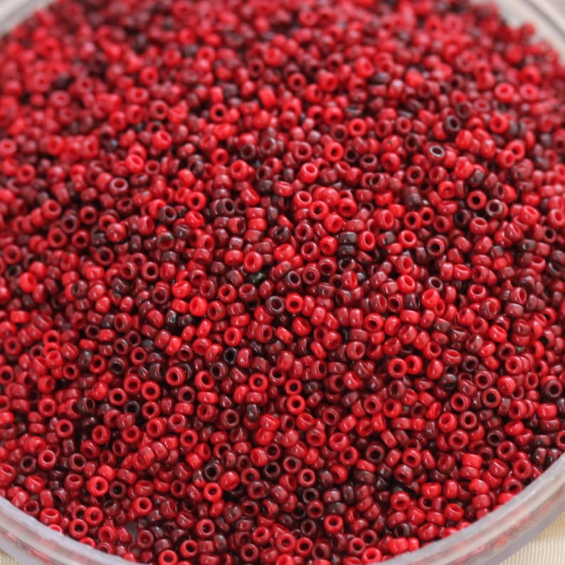 May include: A close-up image of a large quantity of small, round, red and burgundy beads. The beads are arranged in a random pattern and appear to be made of glass or plastic.