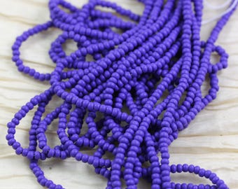 May include: A close-up of a large quantity of small, round, purple beads. The beads are strung together in long strands and are arranged in a pile.