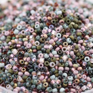 May include: A close-up of a collection of small, colourful beads. The beads are a mix of pastel shades, including pink, green, blue, and gold. They are cylindrical with a central hole, ideal for threading.