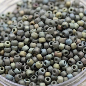 May include: A close-up of a pile of small, round, gray and green glass beads. The beads have a matte finish and are slightly iridescent.
