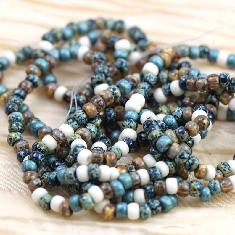 May include: A close-up of a pile of small, colorful glass beads. The beads are a mix of blue, white, and brown, and they have a speckled or marbled appearance.