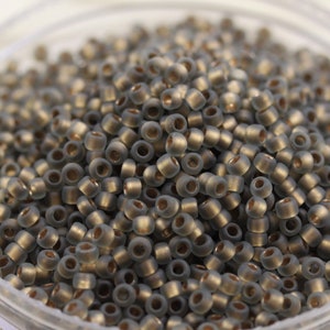May include: A close-up of a container filled with small, round, opaque gray glass beads. The beads have a subtle shimmer and are perfect for jewelry making or crafting.
