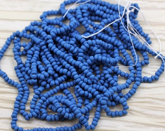 May include: A strand of small, round, matte blue beads. The beads are strung on a white thread and are arranged in a loose pile.