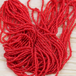 Puede incluir: Primer plano de un montón de cuentas de semillas rojas. Las cuentas son pequeñas y redondas, y tienen un acabado brillante.