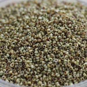 May include: A close-up of a large quantity of small, round, white beads with brown speckles. The beads are arranged in a random pattern and appear to be made of glass or ceramic.