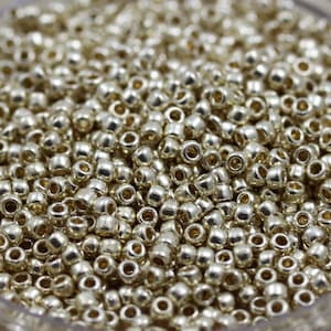 May include: A close-up view of a large quantity of small, round, silver-colored beads. The beads are arranged in a random pattern and appear to be made of metal.