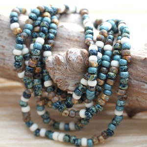 May include: A multi-strand necklace made of small, blue, white, and brown beads. The beads have a speckled pattern and are arranged in a random order.