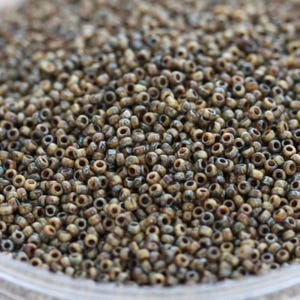May include: A close-up view of a large quantity of small, round, brown seed beads with a subtle blue and white marbling effect.