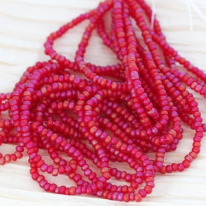 May include: A strand of red iridescent seed beads. The beads are small and round, and they have a subtle shimmer to them.