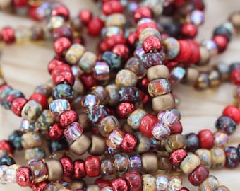 May include: A close-up of a strand of beads in shades of red, brown, and gold. The beads are made of glass and have a variety of textures and finishes.
