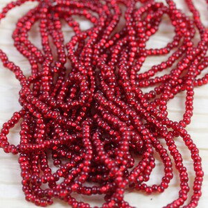May include: A close-up of a pile of red seed beads. The beads are small and round, and they have a shiny finish.