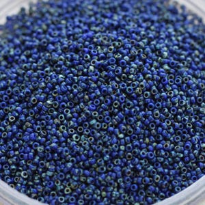 May include: A close-up view of a large quantity of small, round, blue glass beads. The beads have a slightly iridescent finish, giving them a subtle sparkle.