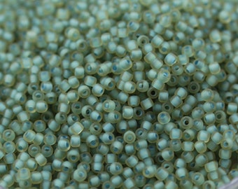 May include: A close-up view of a large quantity of small, opaque, light green glass beads. The beads are round and have a slightly frosted finish.