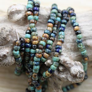 May include: A strand of small, colorful glass beads in shades of blue, brown, and gold. The beads have a speckled, marbled effect and are strung together on a clear thread.