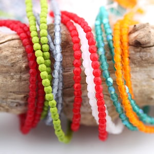 Peut inclure: Assortiment de perles de verre colorées en rouge, vert, blanc, orange et bleu. Les perles sont petites et rondes, et elles sont enfilées sur une ficelle.