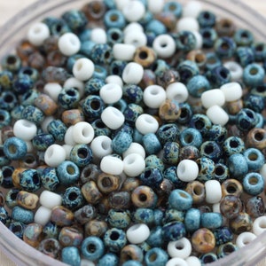 May include: A close-up of a bowl filled with small, round beads. The beads are a mix of white, blue, and brown colors. The beads have a speckled or marbled appearance.