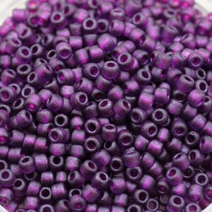 May include: A close-up view of a large quantity of small, round, purple glass beads. The beads have a frosted, matte finish and a slight sparkle.