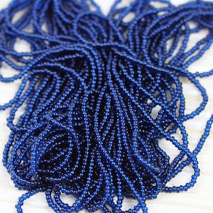 May include: A close-up of a pile of small, round, dark blue glass beads. The beads are arranged in a random pattern and are all the same size.