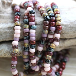 May include: A strand of multi-colored seed beads in shades of pink, brown, gold, and black. The beads are arranged in a repeating pattern.