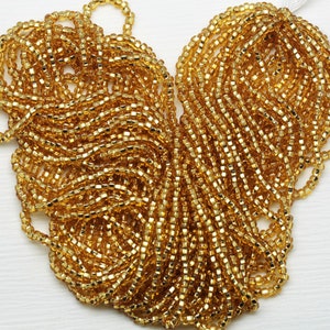 May include: A large quantity of gold seed beads, arranged in a heart shape. The beads are small and have a shiny, metallic finish.