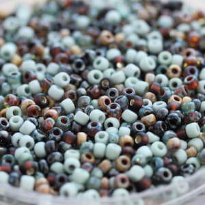 May include: A close-up of a variety of small, round beads in shades of blue, brown, and beige. The beads are arranged in a random pattern, creating a visually appealing texture.
