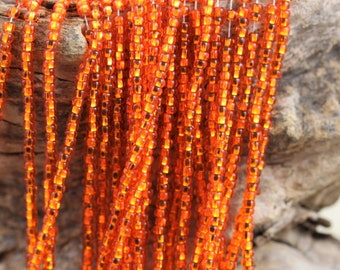 May include: A strand of orange seed beads. The beads are small and round, and they are strung on a clear thread.