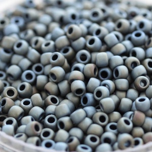 Może przedstawiać: Widok z bliska dużej ilości małych, okrągłych, szarych koralików. Korale mają matowe wykończenie i delikatny, tęczowy połysk.