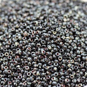 May include: A close-up of a pile of black seed beads with white and red speckles. The beads are small and round, and they are perfect for jewelry making.