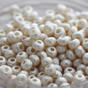 May include: A close-up of a pile of white pearl-like beads. The beads are round and have a smooth, shiny finish.